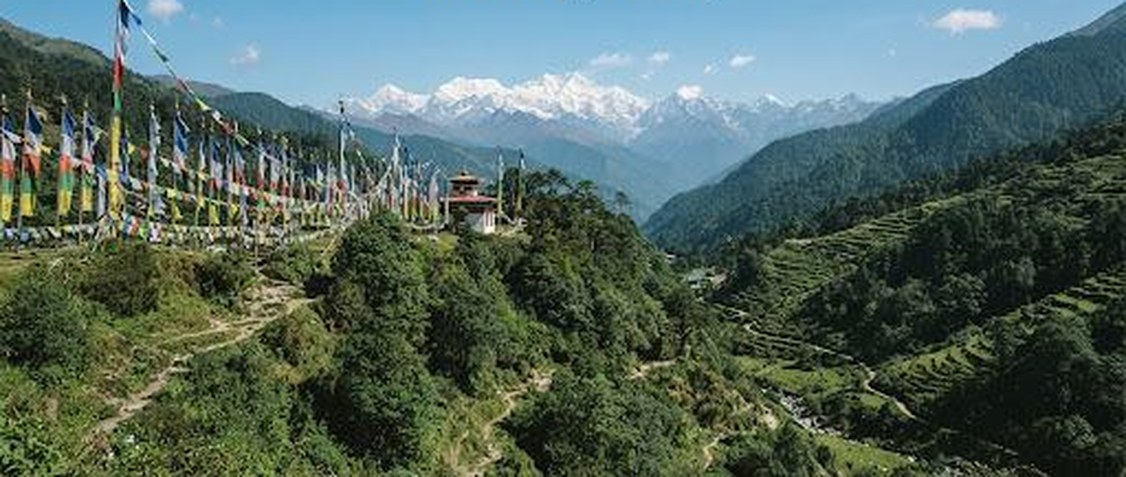 Prayer flags above a Sikkim valley with snow-capped Himalayan peaks in the distance